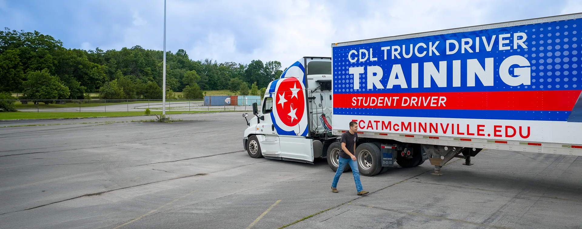 Person walking past a CDL training truck with large &ldquo;TRUCK DRIVER TRAINING&rdquo; and &ldquo;CATMcMINNVILLE.EDU&rdquo; text in parking lot