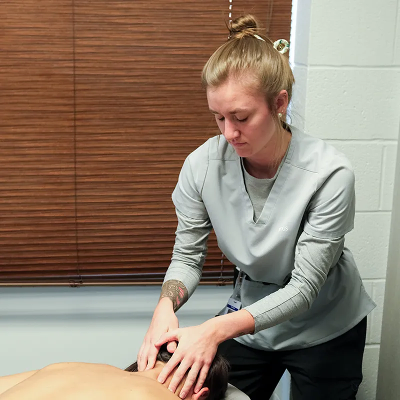 Student performing massage on a person lying face down on a table in a room with closed blinds
