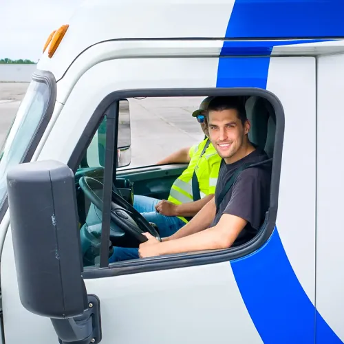 Person seated in truck cab at steering wheel while another person in safety vest sits in passenger seat