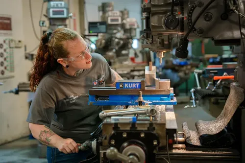 Person adjusting metal piece on milling machine with vise and cutting tool in shop