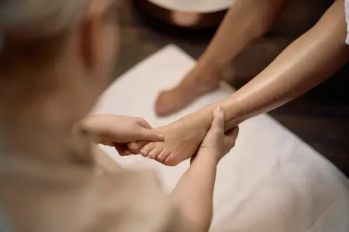 Hands applying pressure to a foot during a reflexology treatment while the person&rsquo;s lower leg rests on a white towel.